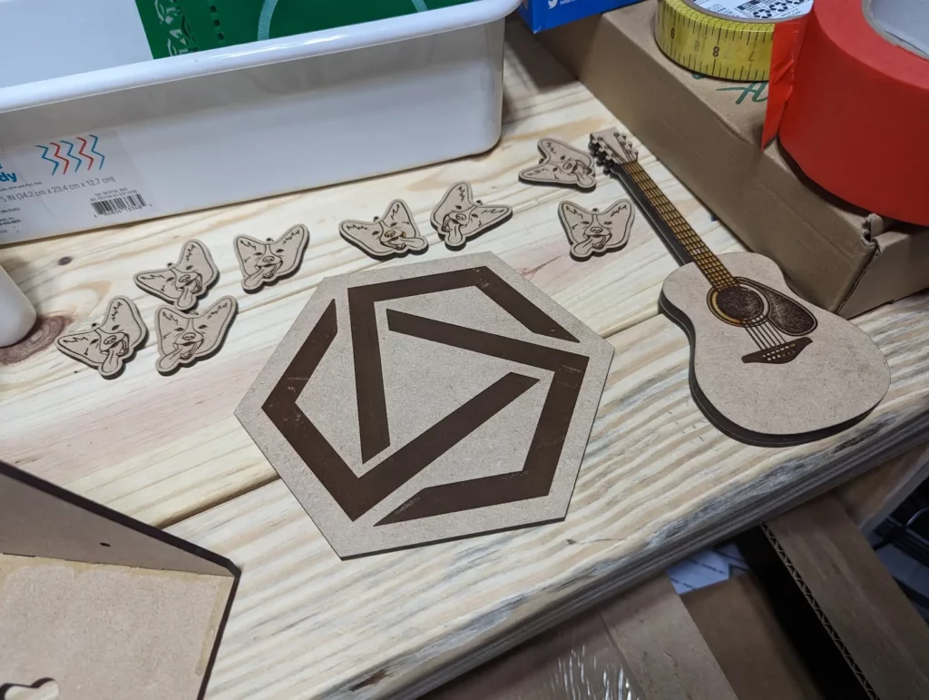 Laser cut samples including a logo for the Agent Academy, A guitar pick holder that looks like a guitar, and multiple corgi earrings created by The Eclectric co.
